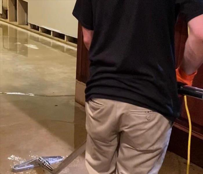 man in khaki pants and SERVPRO shirt vacuuming water off of concrete floors