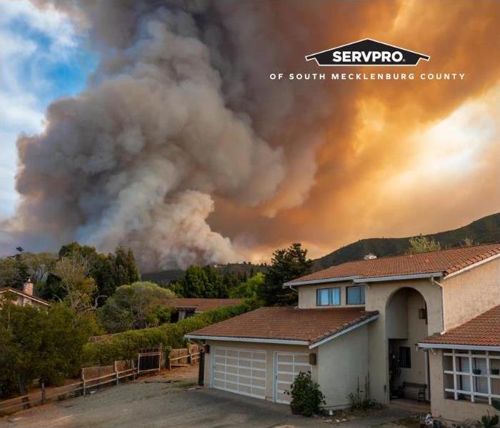 Photo of a house in a neighborhood with smoke billowing in the distance from a wildfire